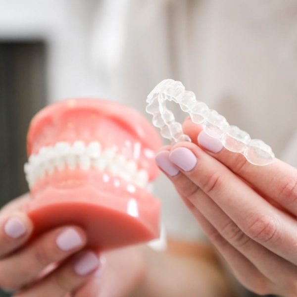 orthodontist holding an invisalign clear aligner in one hand and a plastic model in the other