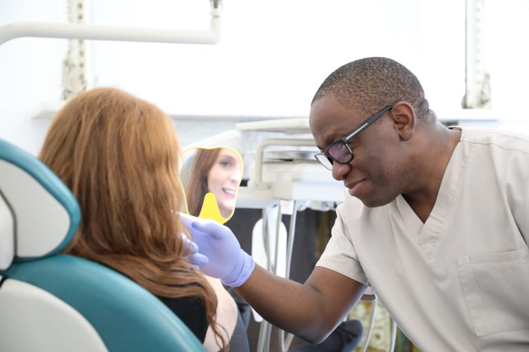 Luxation Injuries Treatment for Displaced Teeth Specialists showing their female patient their Luxation Injuries Treatment for Displaced Teeth Results who is happy and smiling looking in the mirror with her new Luxation Injuries Treatment for Displaced Teeth