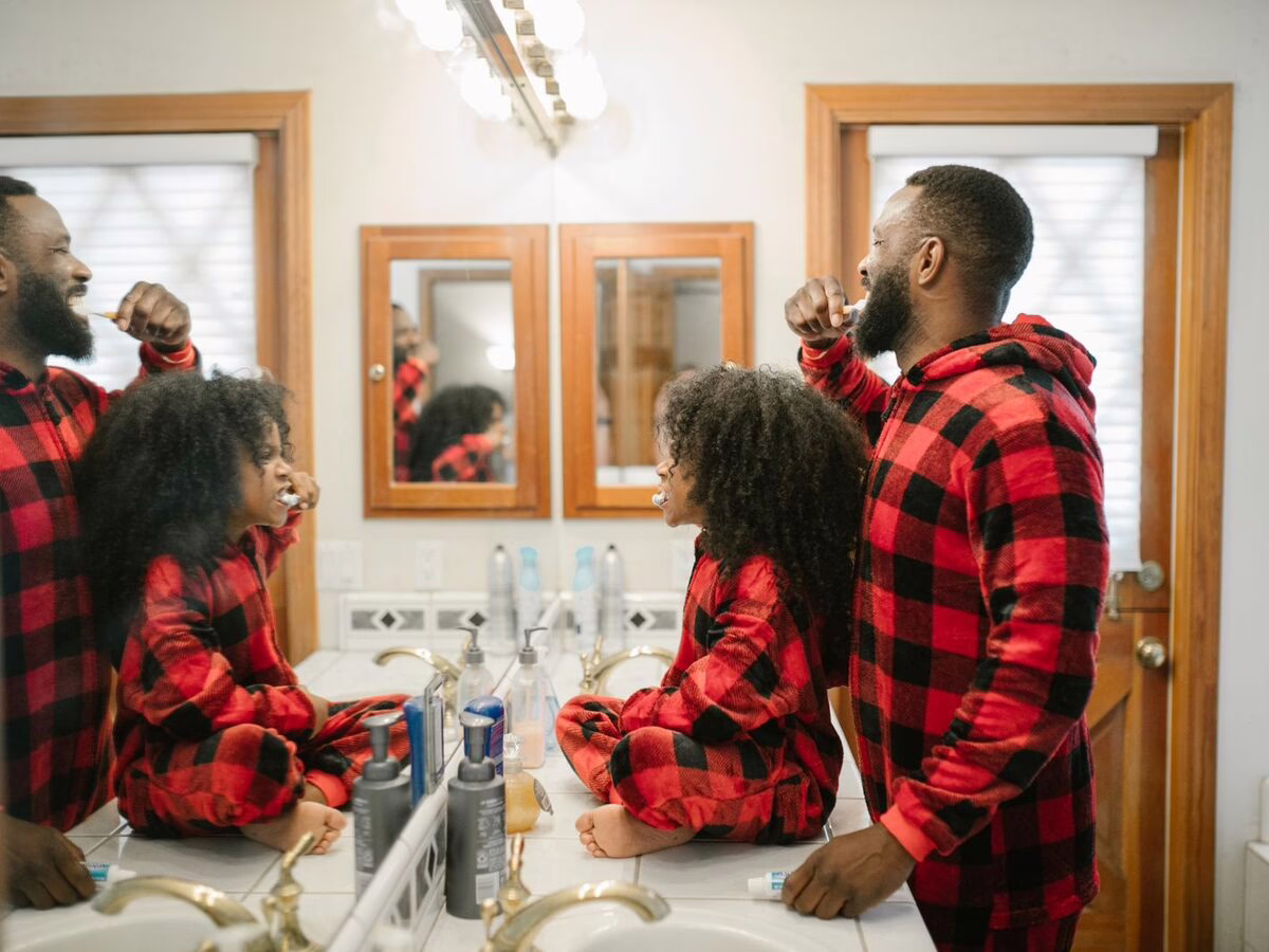 A parent and child brushing their teeth at the mirror