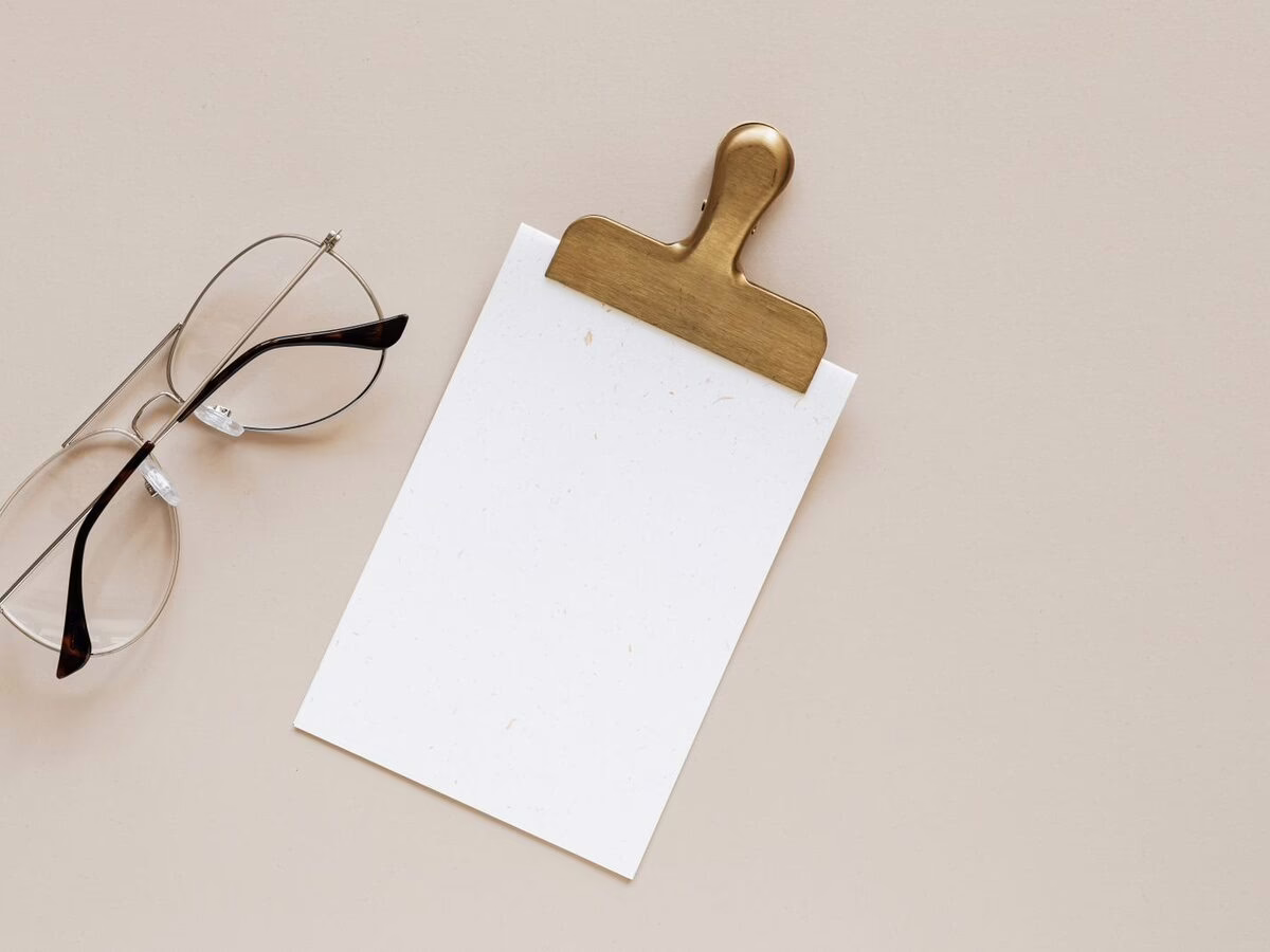 A blank notepad on a clipboard beside a pair of glasses