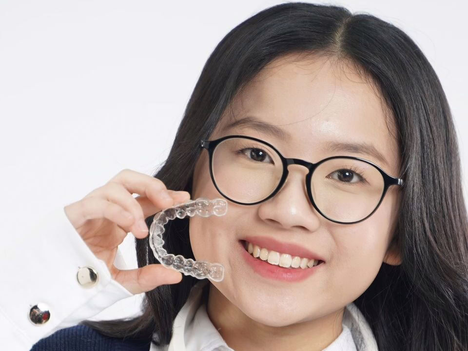 A teenager in school uniform holding a clear aligner and case
