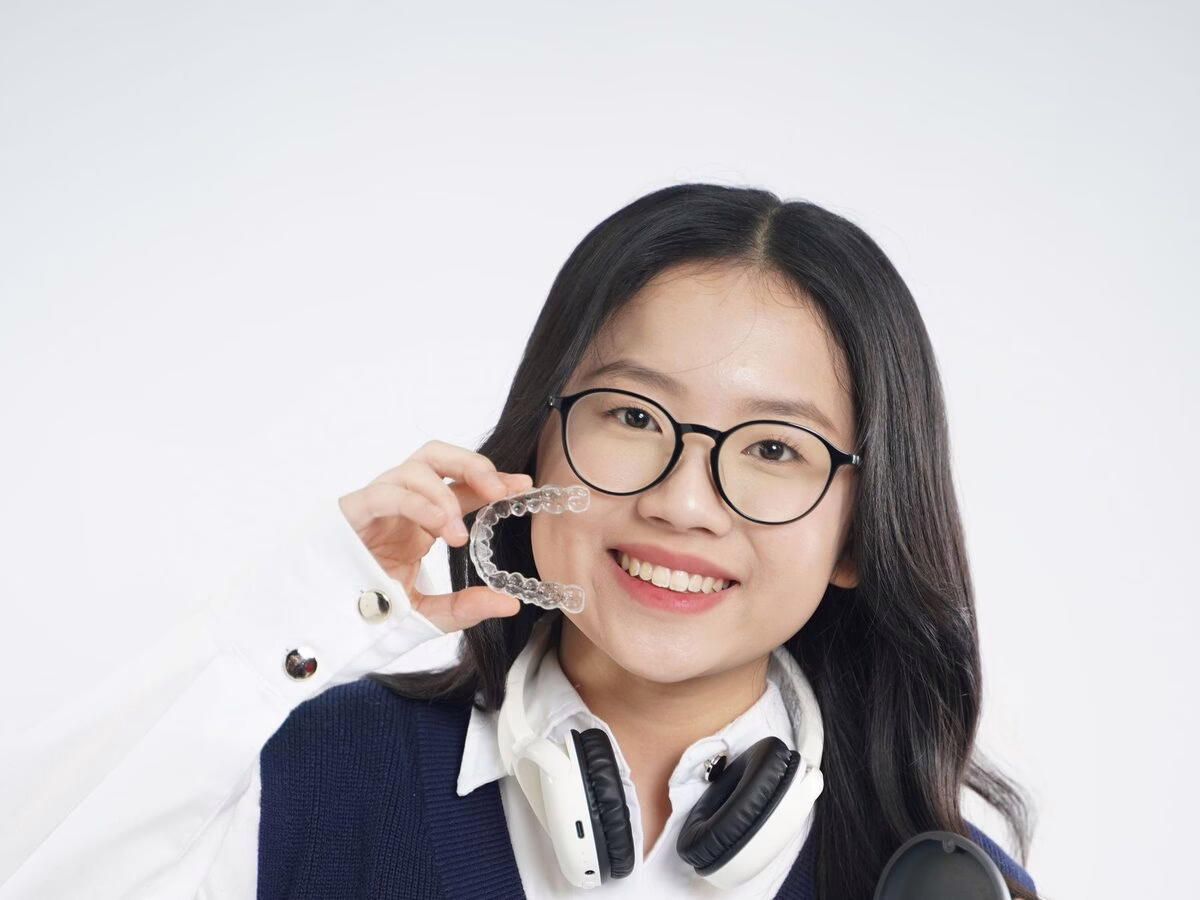 A teenager in school uniform holding a clear aligner and case