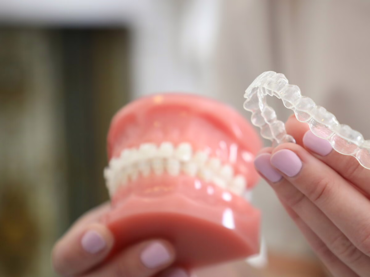 A clear aligner held beside a dental model with braces