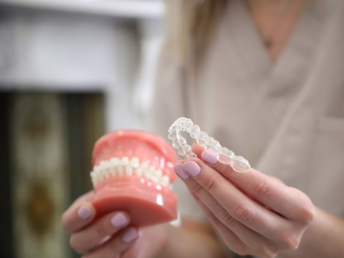 A clear aligner held beside a dental model with braces