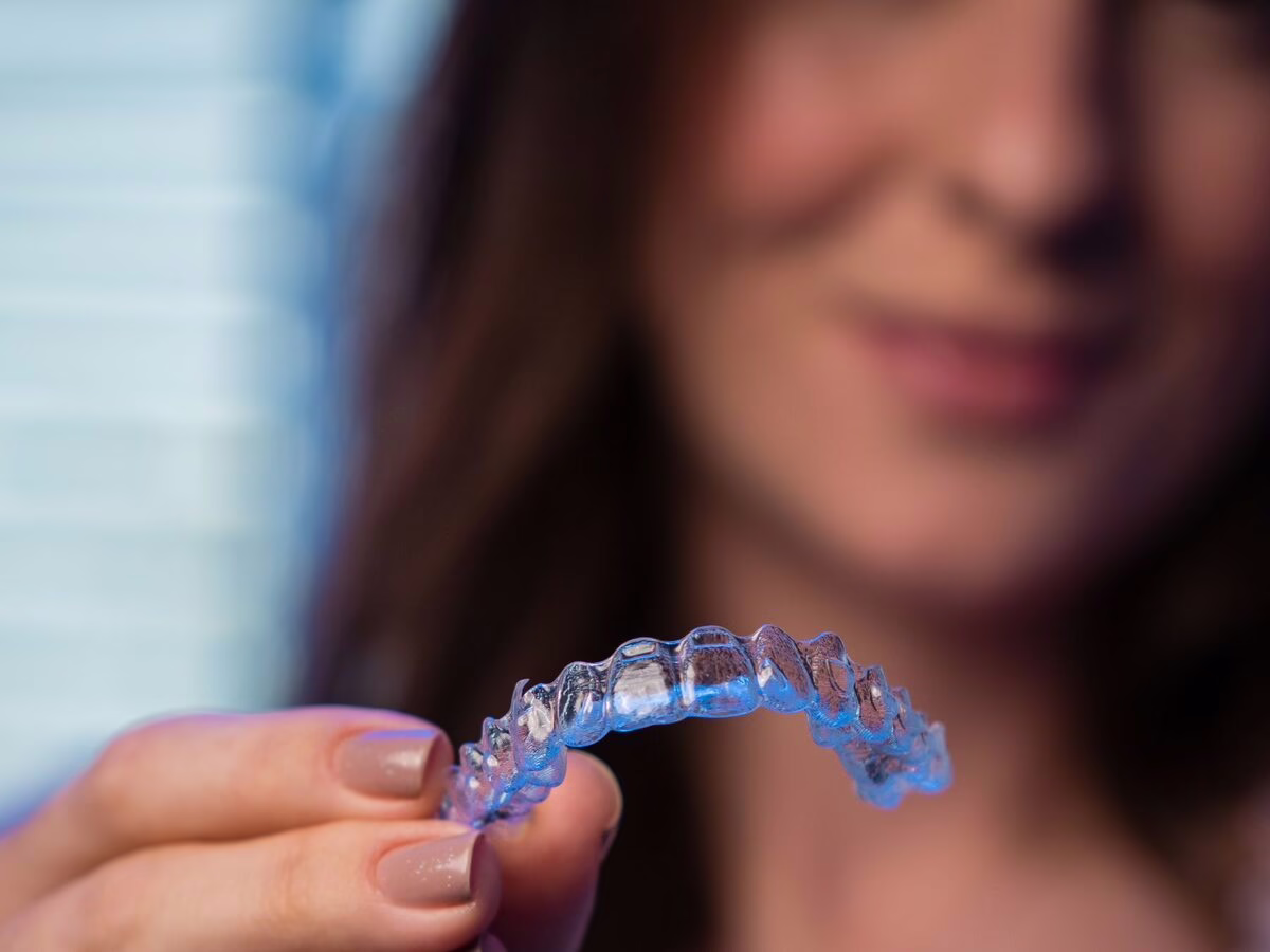 A clear aligner held up to the mouth