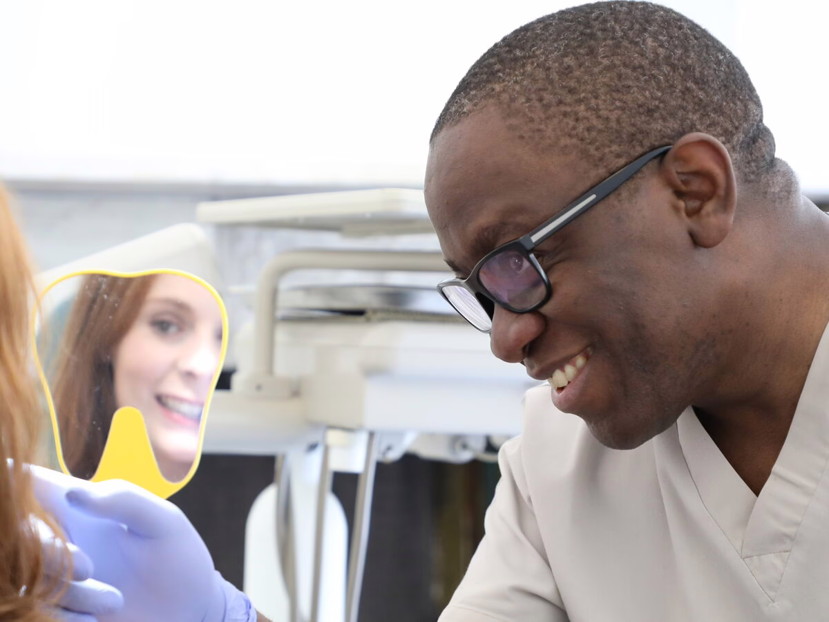 Dr Ope Sodeinde showing a patient her smile in a hand mirror