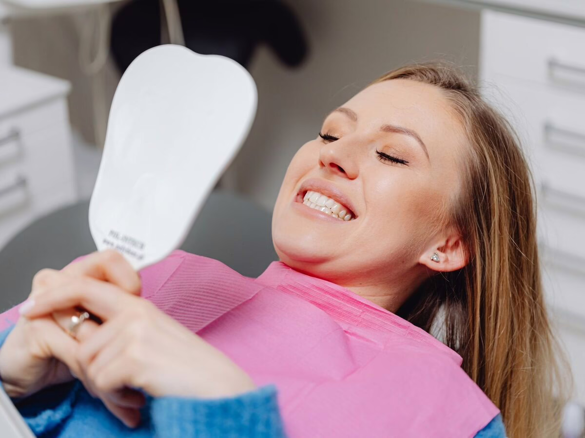 A patient checking her smile in a hand mirror in the dental chair
